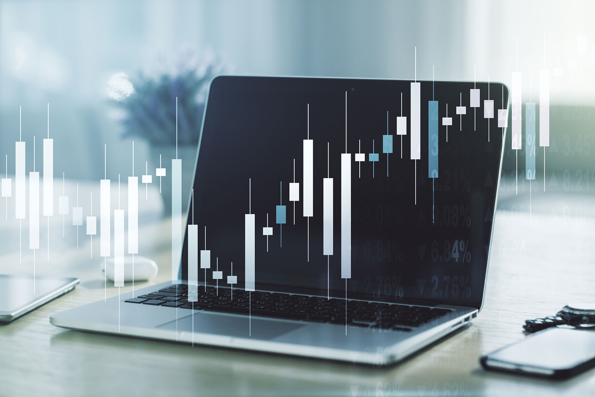 A laptop on a desk with a blurry background, overlaid with digital candlestick chart graphics representing financial data or stock market analysis.